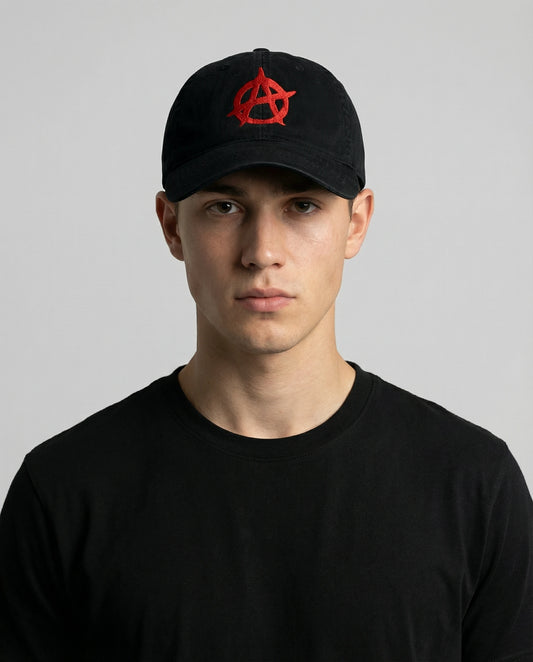 Male model wearing 999TEE Anarchy 001 black dad cap with red embroidered logo, styled in a dark studio setting for a bold streetwear look
