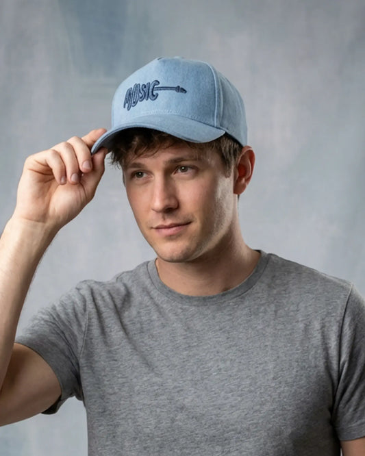 Male model wearing a blue denim baseball cap with “Music” embroidery, styled with a gray t-shirt against a neutral studio background.