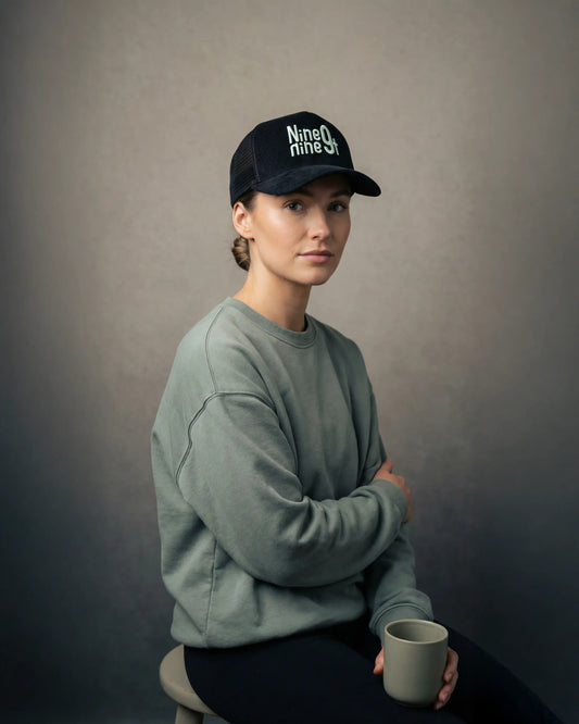 Female wearing black trucker cap with Nine9ninet logo, seated model shot