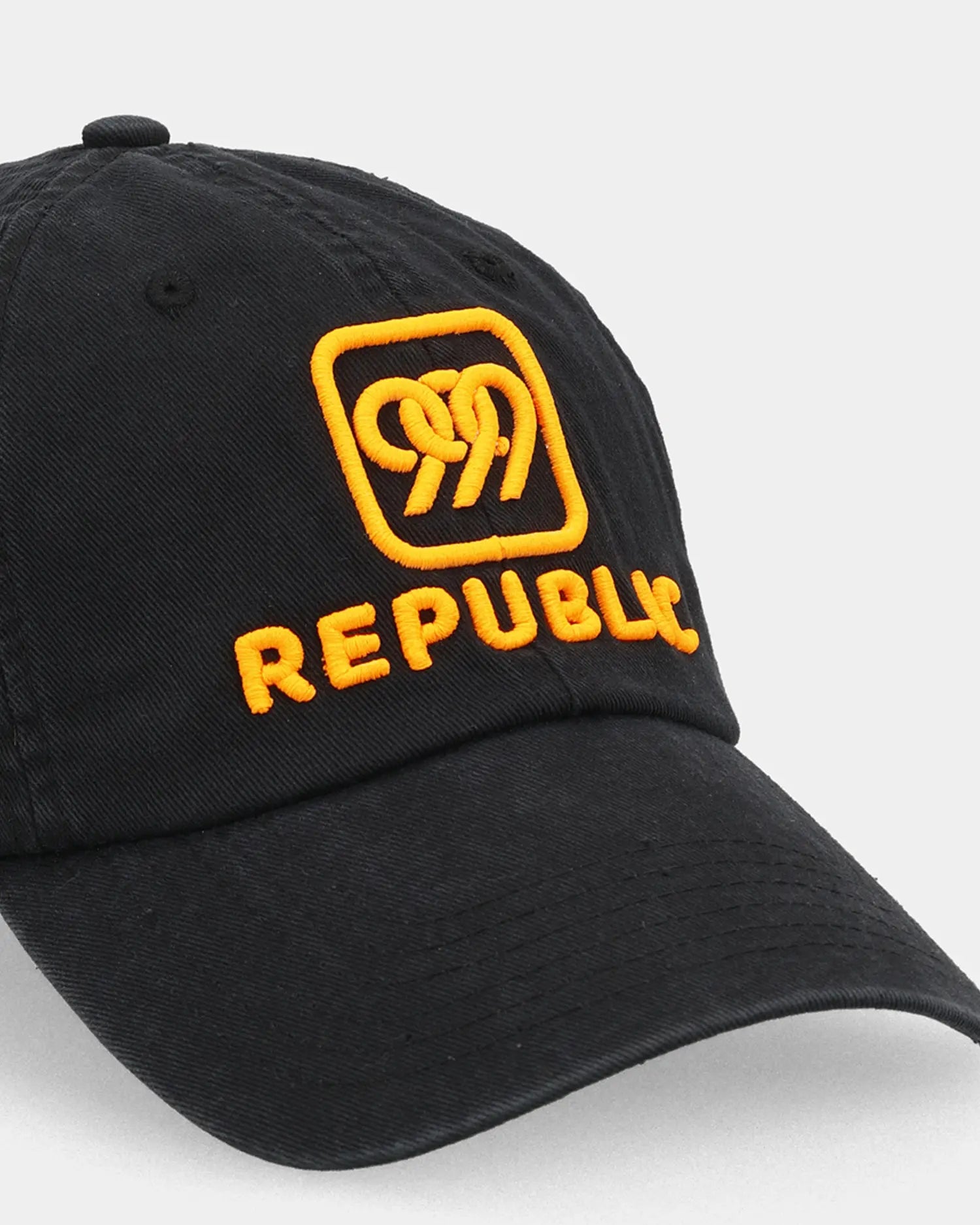 Black dad cap with orange REPUBLIC embroidery, angled front detail view