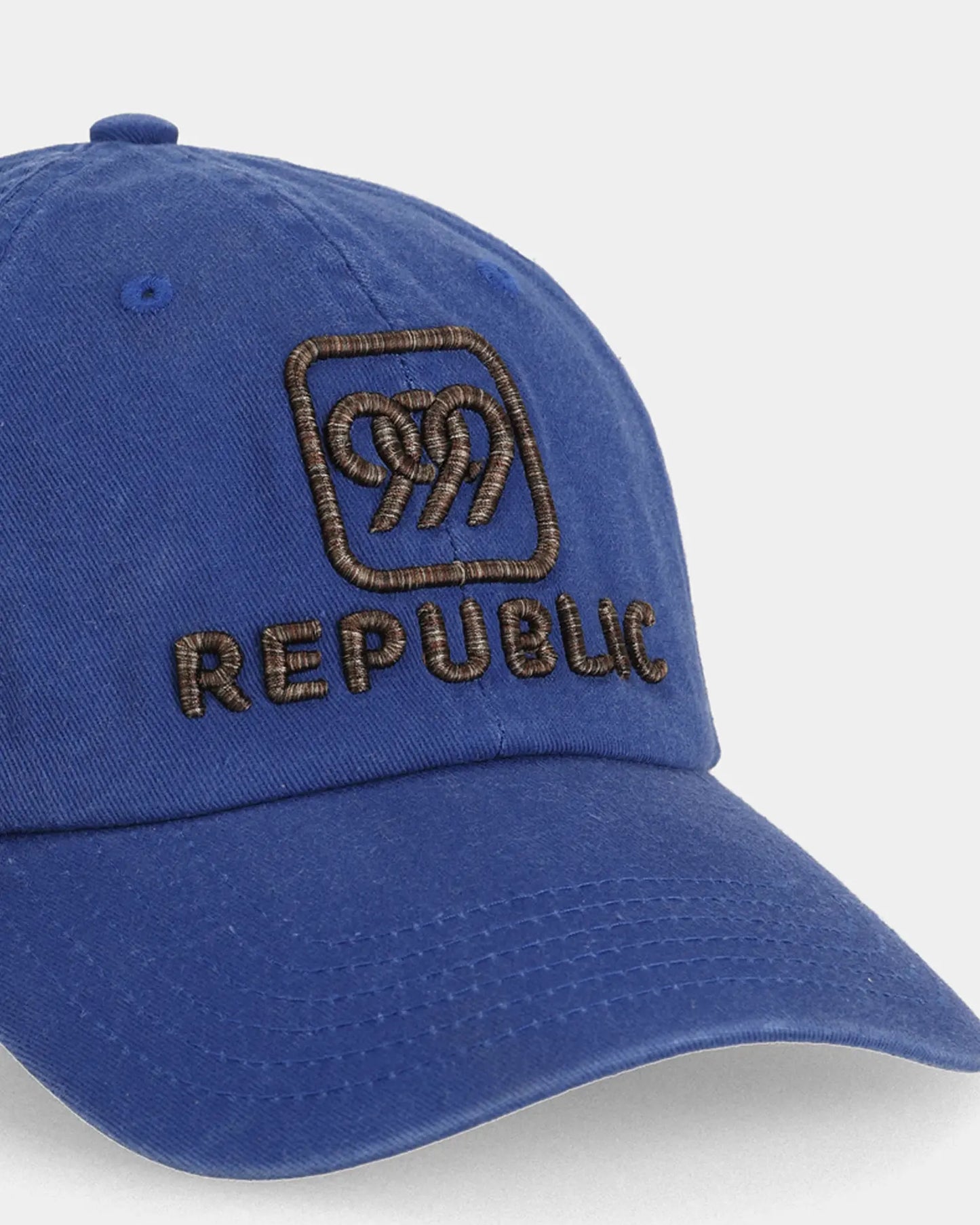 Blue dad cap with multibrown REPUBLIC embroidery, angled close-up product shot
