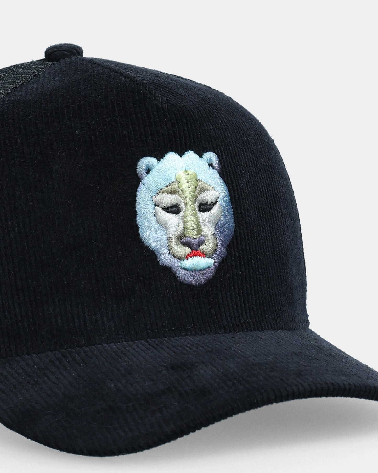 Black corduroy trucker cap with blue lion face 3D embroidery, angled close-up product shot
