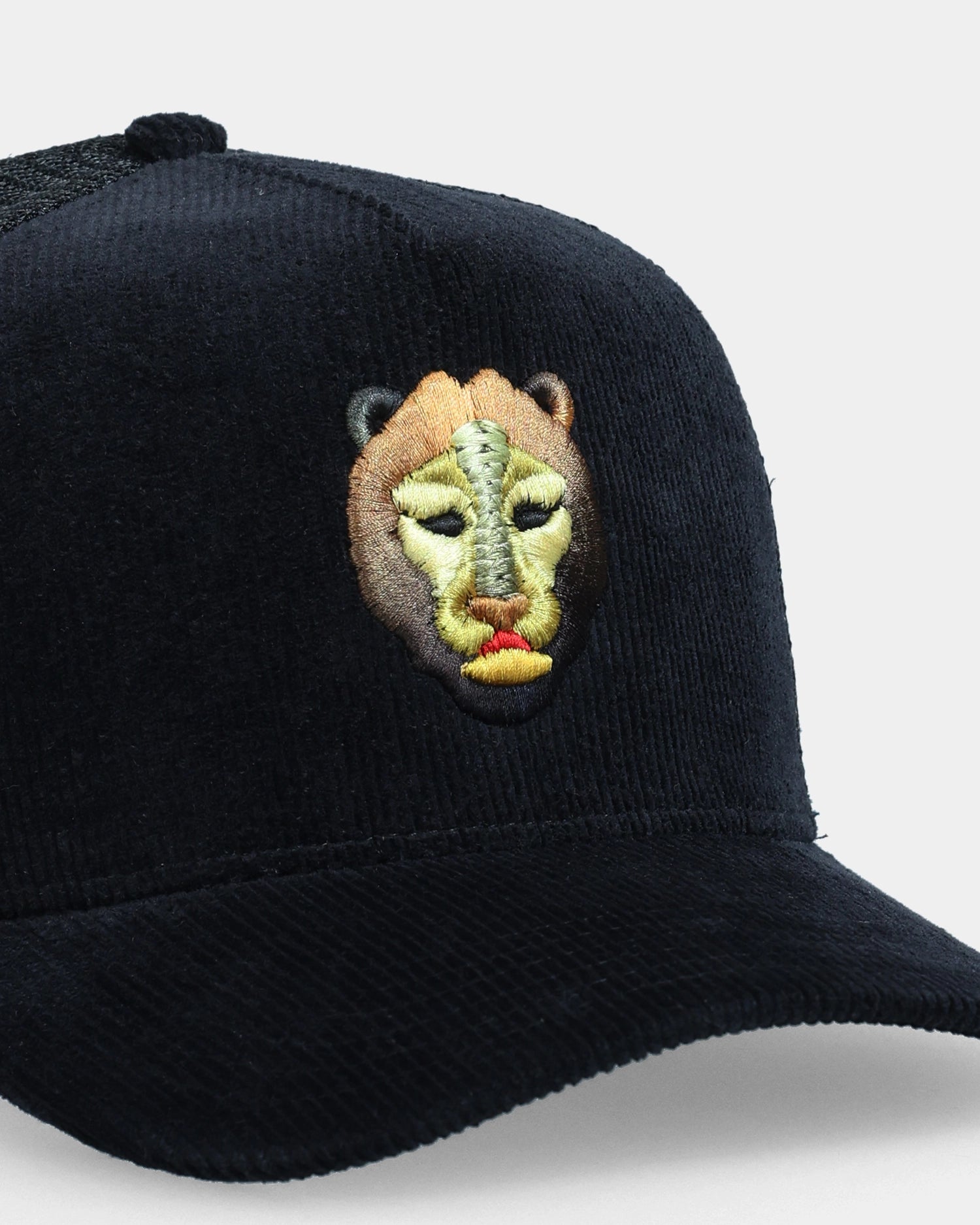 Black corduroy cap with lion face embroidery, angled close-up product shot
