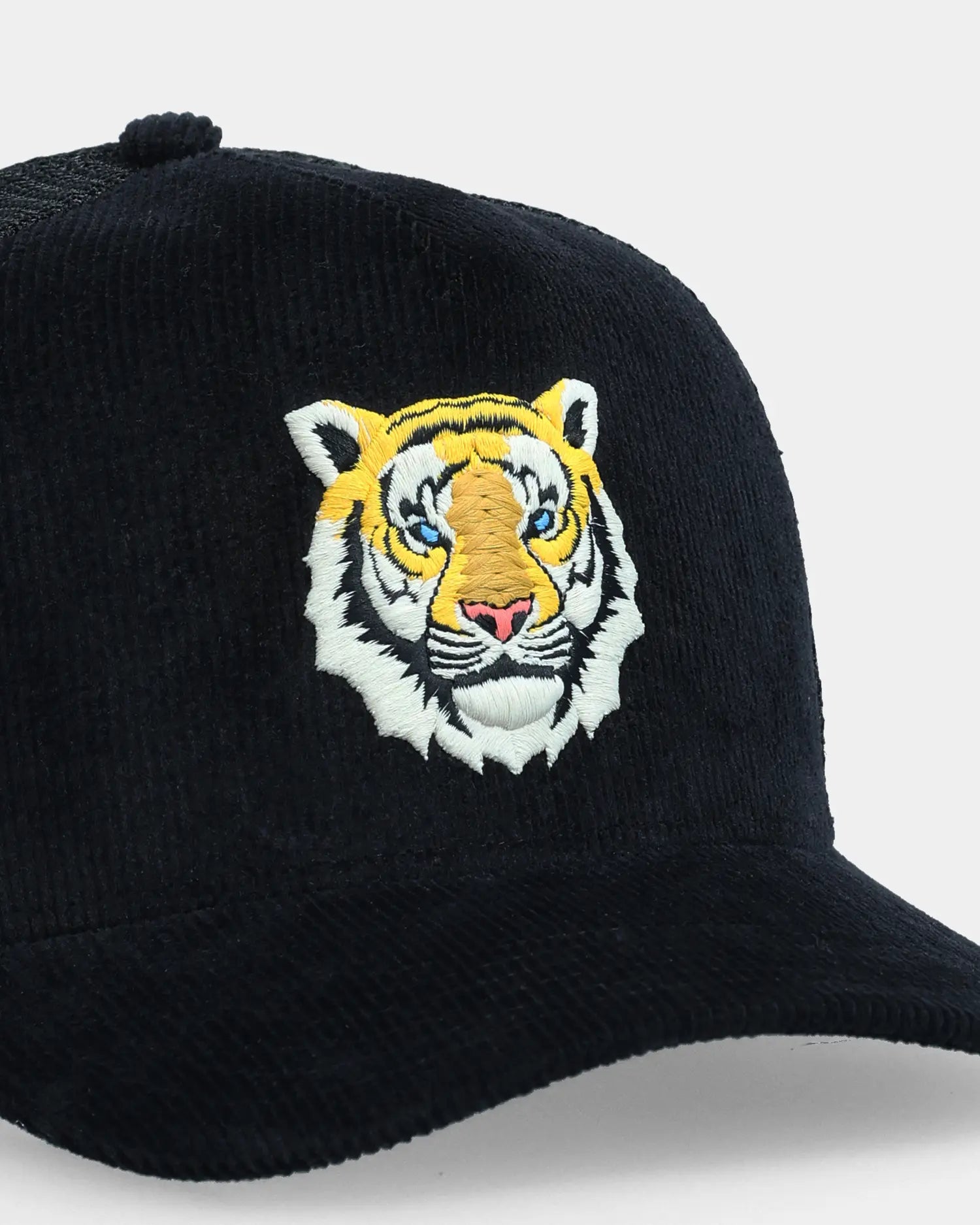 Black corduroy trucker cap with tiger face embroidery, angled close-up product shot
