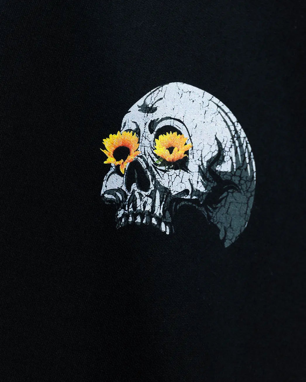 Black oversized t-shirt with cracked skull graphic and yellow flower eyes, close-up print view