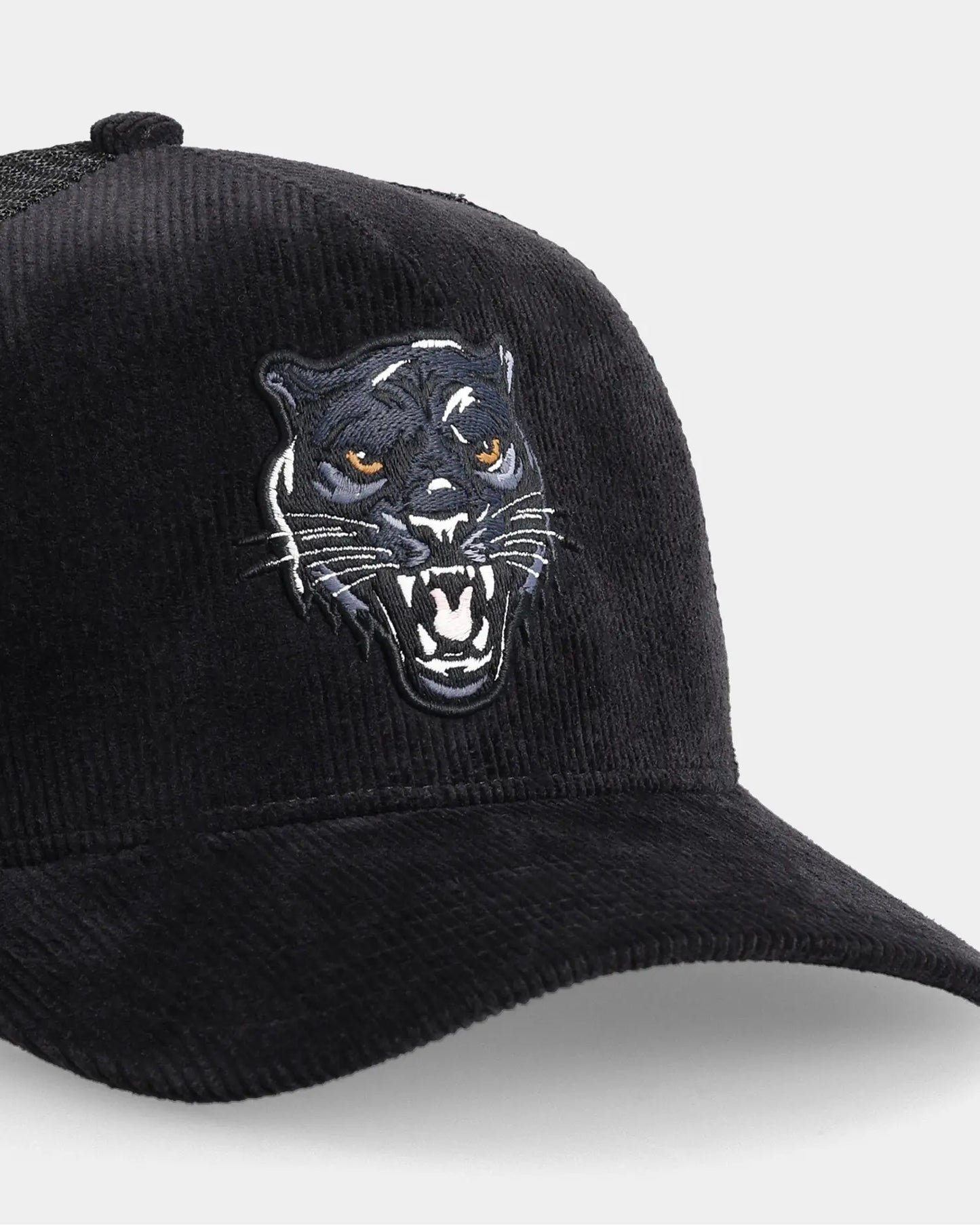 Black corduroy trucker cap with panther head embroidery, angled close-up product shot
