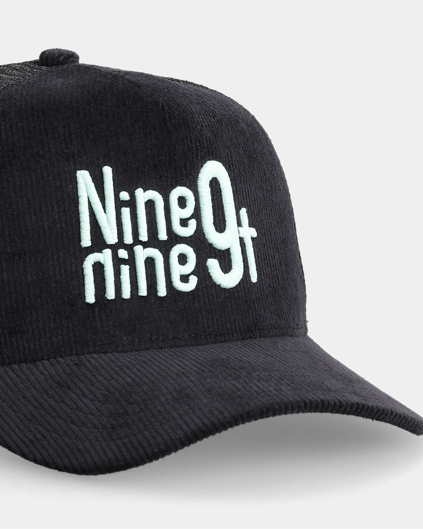 Black trucker cap with Nine9ninet embroidery, angled close-up product shot
