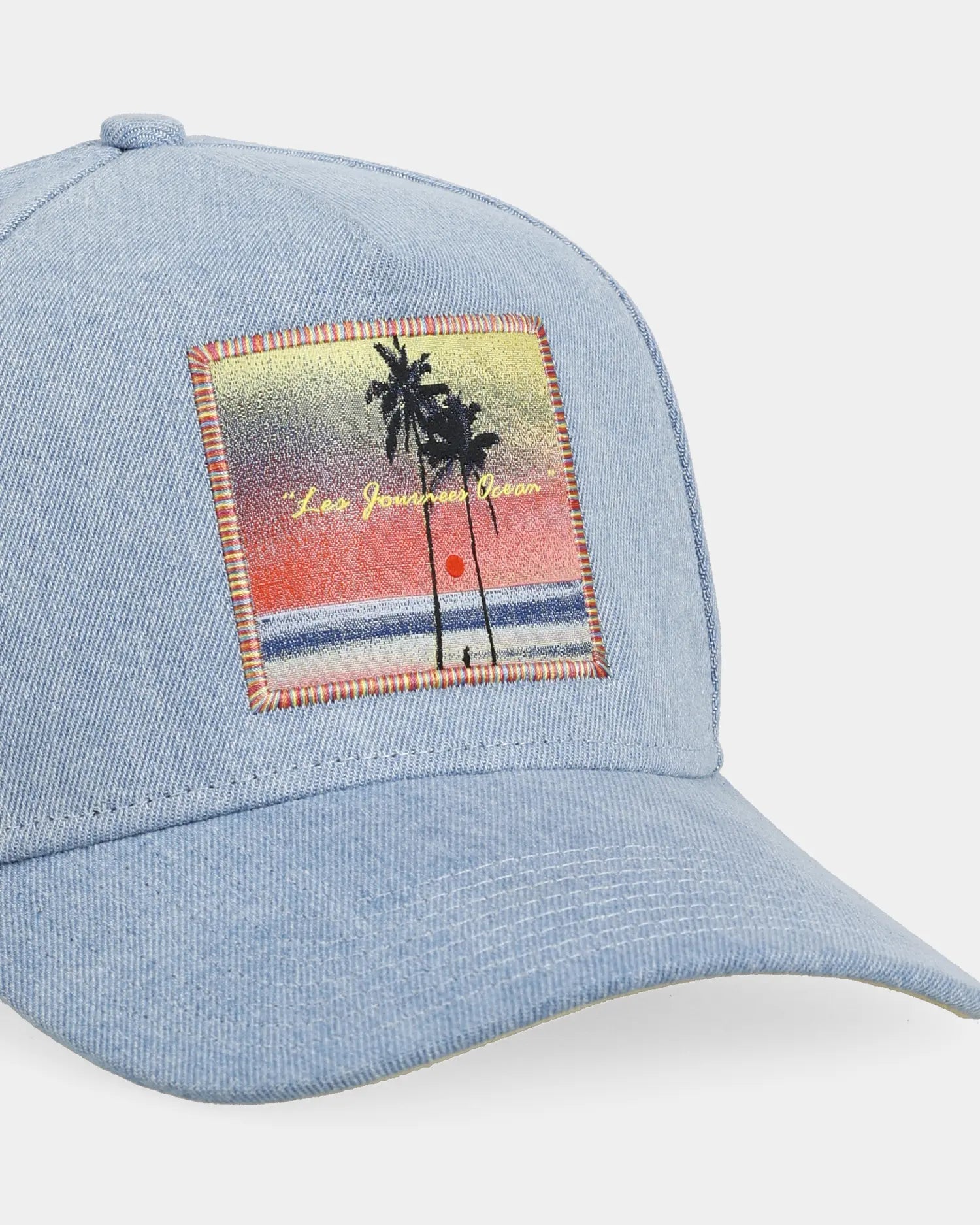 Blue denim cap with beach patch, angled front close-up detail
