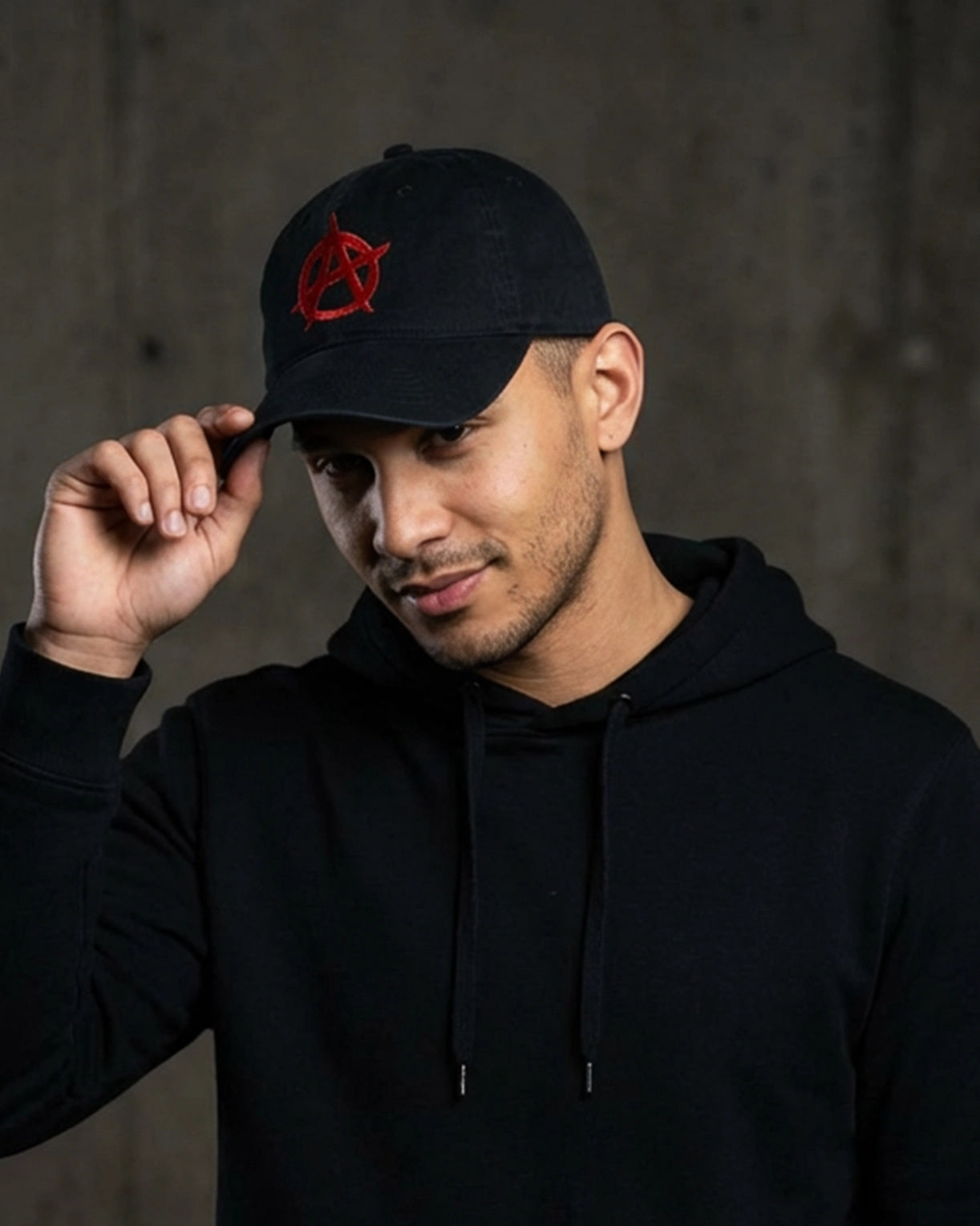Male model wearing 999TEE Anarchy 001 black dad cap with red embroidered logo, styled in a dark studio setting for a bold streetwear look