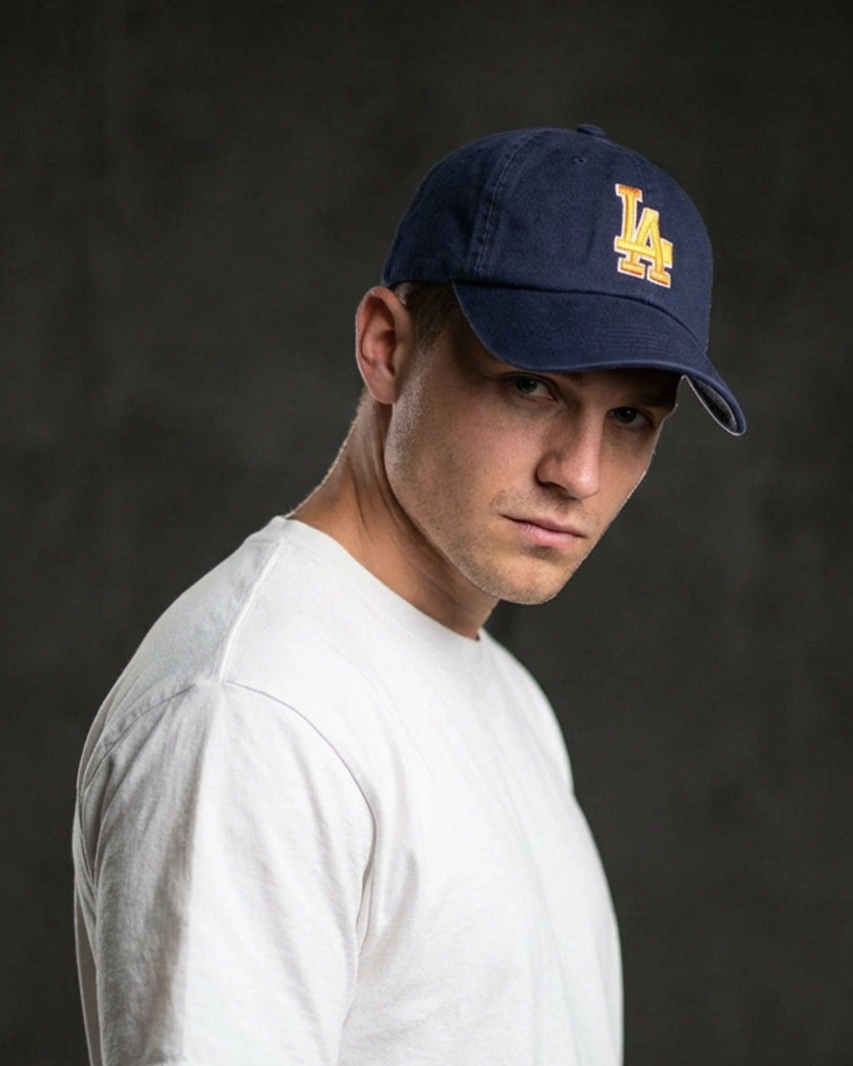 Male model wearing 999TEE LA-01 navy dad cap with embroidered logo, styled in a dark studio setting for a clean premium streetwear look