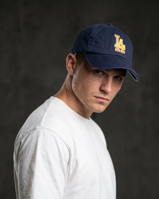 Male model wearing 999TEE LA-01 navy dad cap with embroidered logo, styled in a dark studio setting for a clean premium streetwear look
