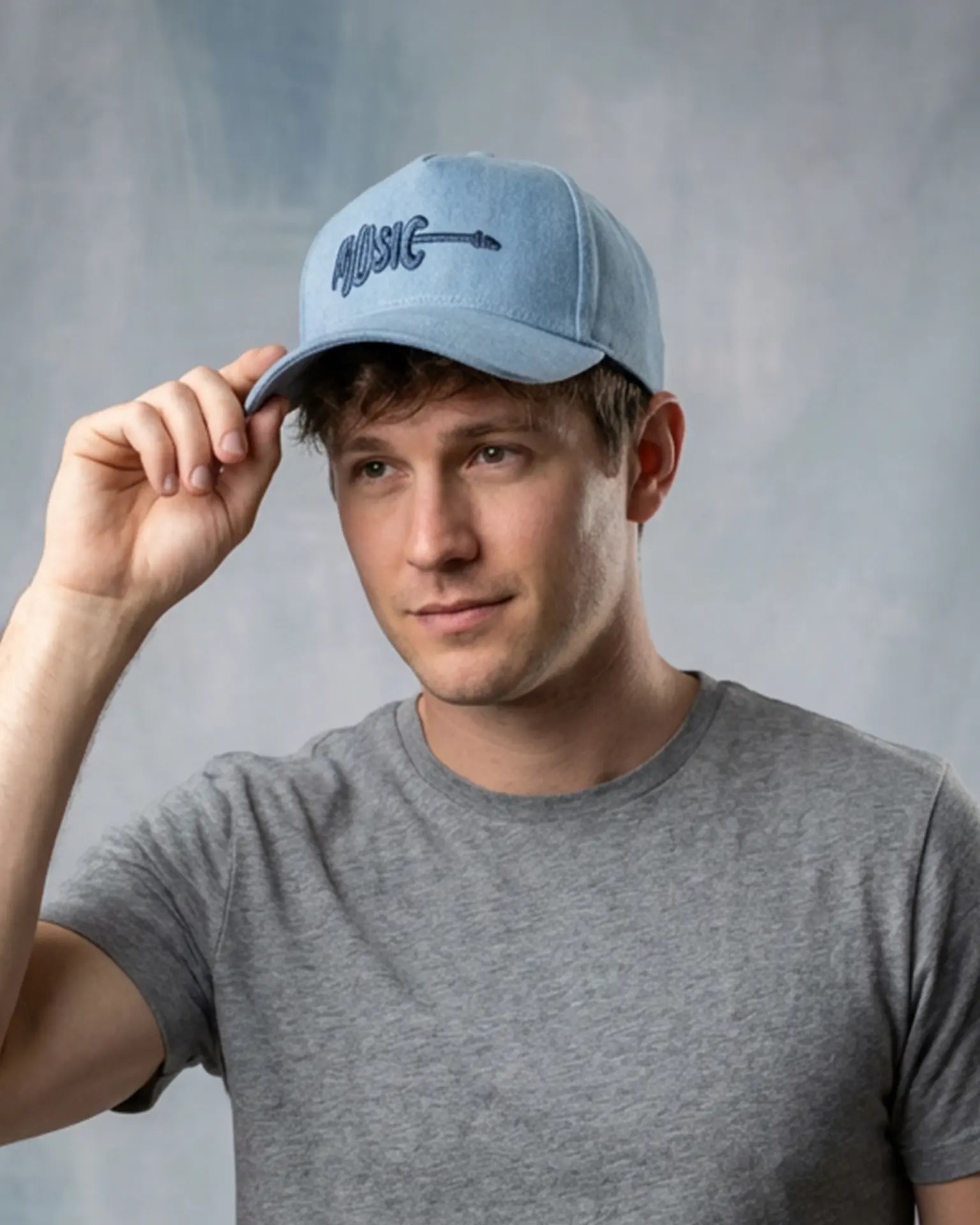 Male model wearing a blue denim baseball cap with “Music” embroidery, styled with a gray t-shirt against a neutral studio background.