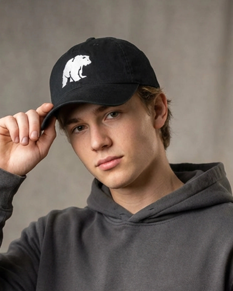 Male model wearing a black dad cap with polar bear embroidery, styled with a gray hoodie against a neutral studio background.