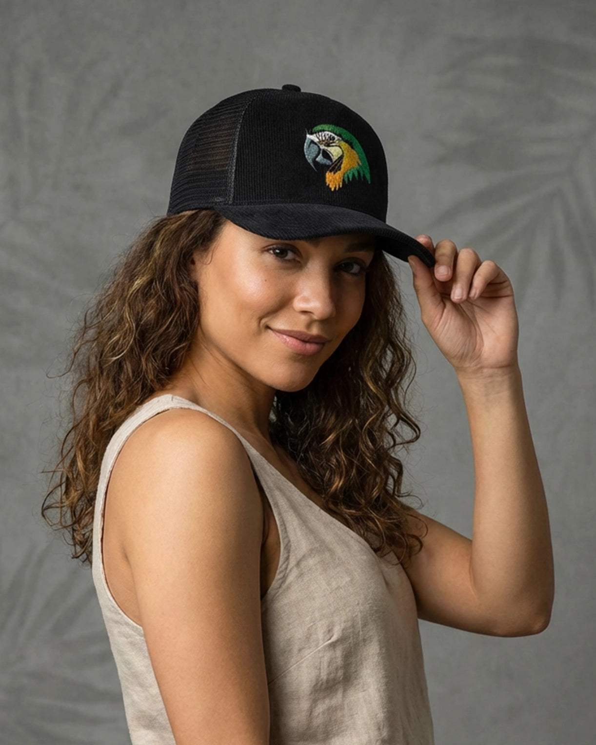 Female model wearing 999TEE Tropical Breeze black trucker cap with embroidered logo, styled against a neutral grey studio background for a clean streetwear look