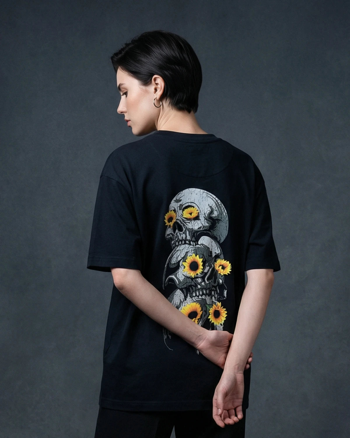 Female model wearing black T-shirt with skull and sunflower graphic, back view