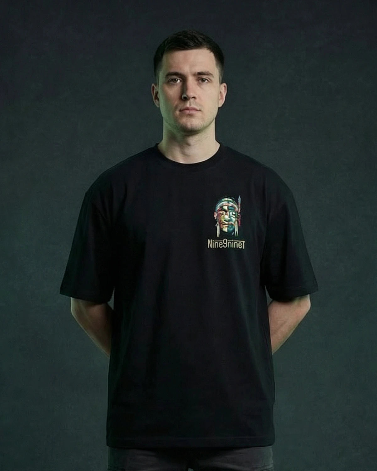 Male model wearing black T-shirt with mask face chest graphic, front view
