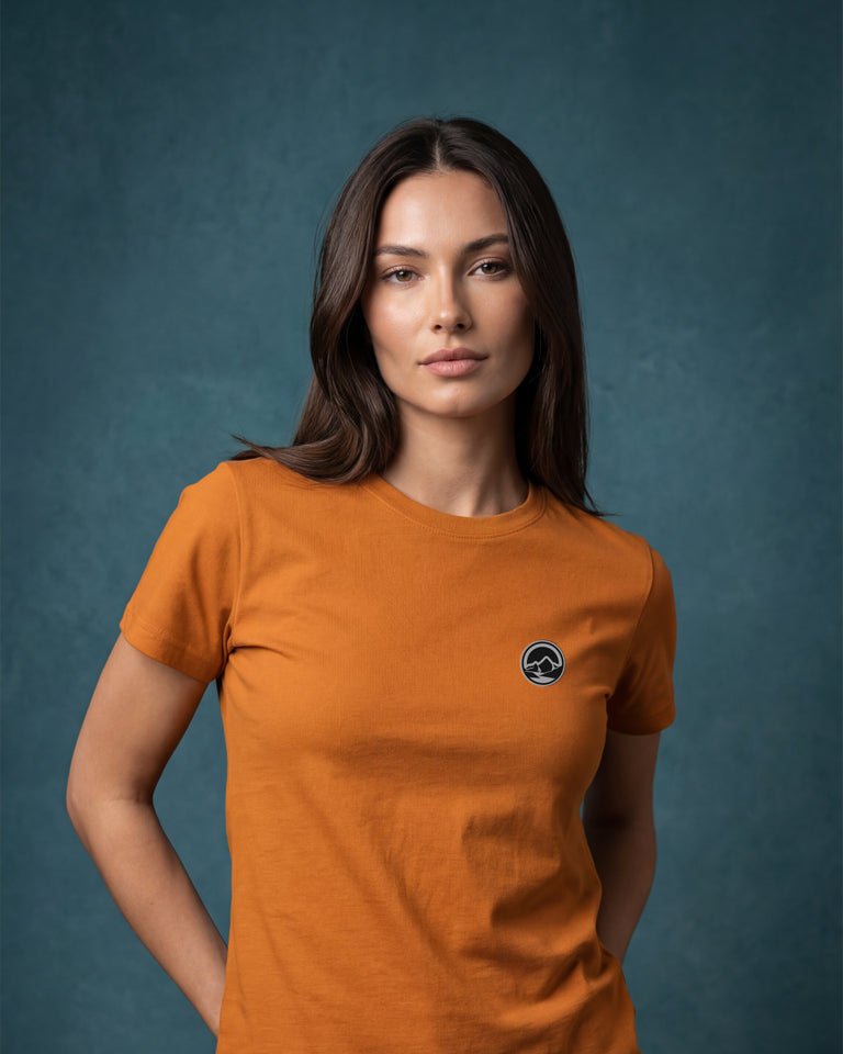 Female model wearing burnt orange T-shirt with small chest logo portrait view