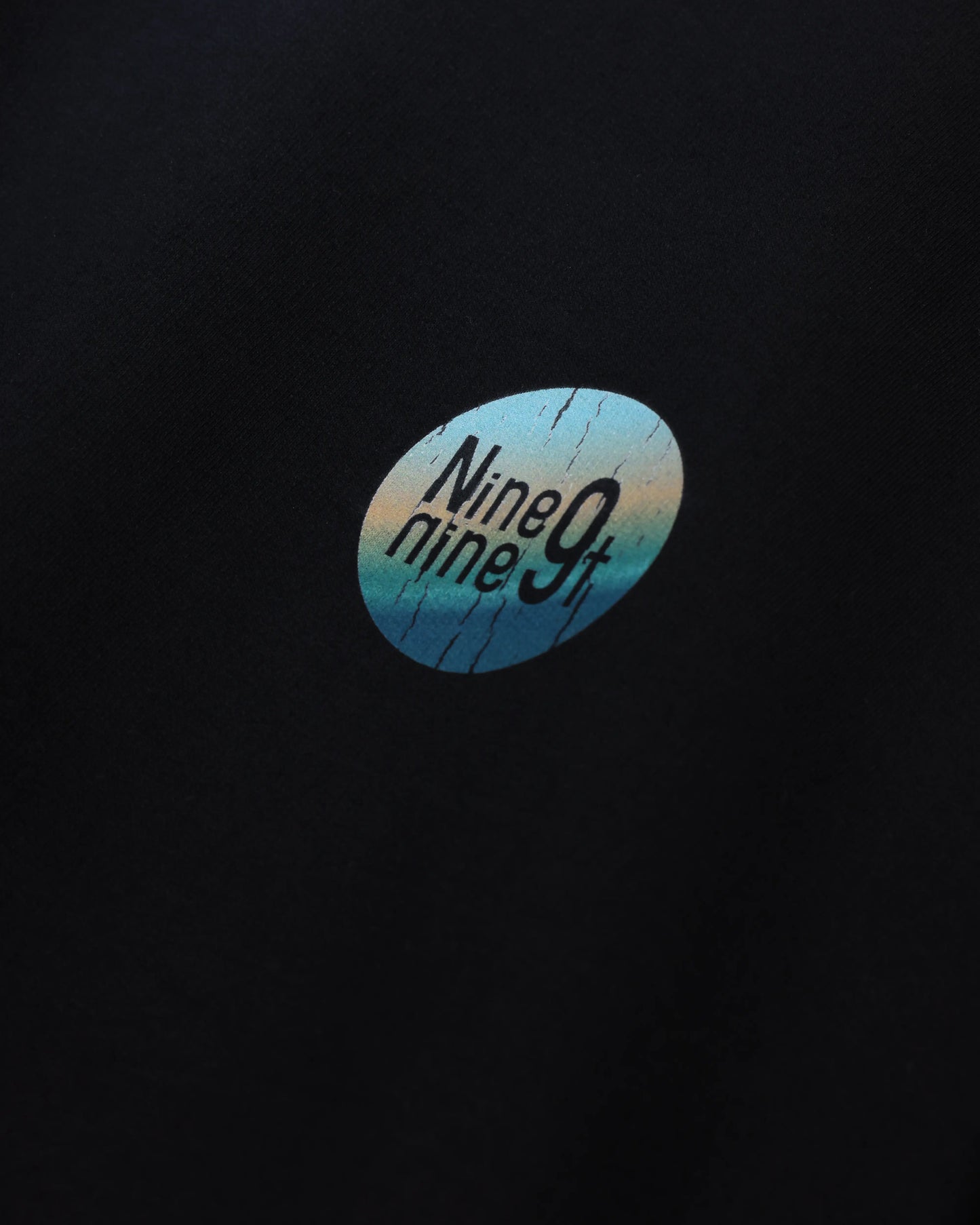 Black T-shirt with Nine9nineT circle chest graphic, close-up detail view
