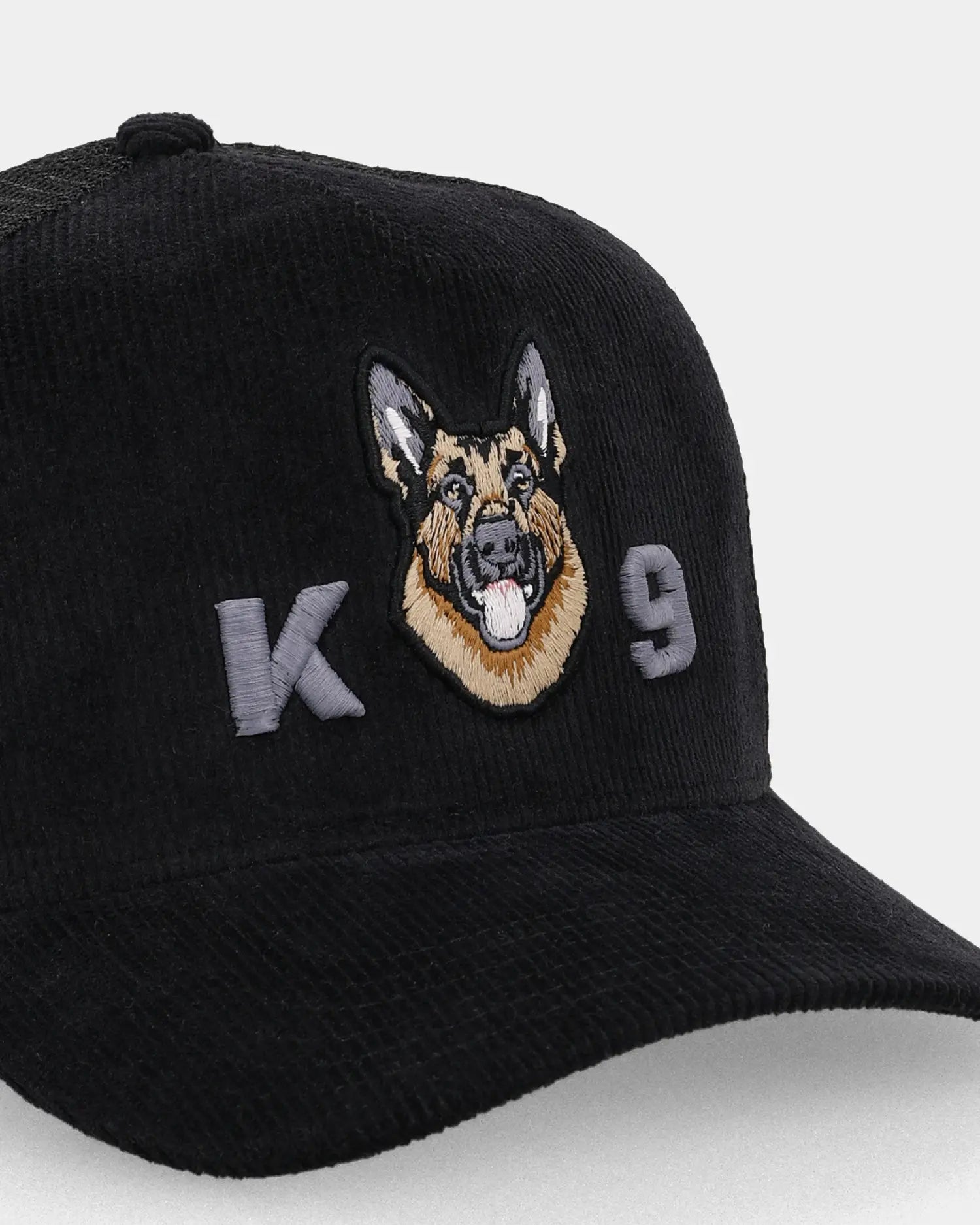 Black corduroy trucker cap with K9 dog embroidery, angled close-up product shot
